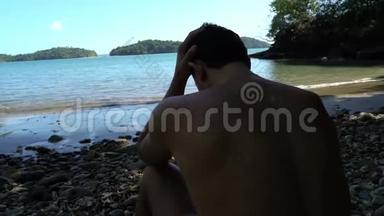 在海边的麻烦人。 年轻人坐在海滩上，看上去很担心。 他抓住了他的头。